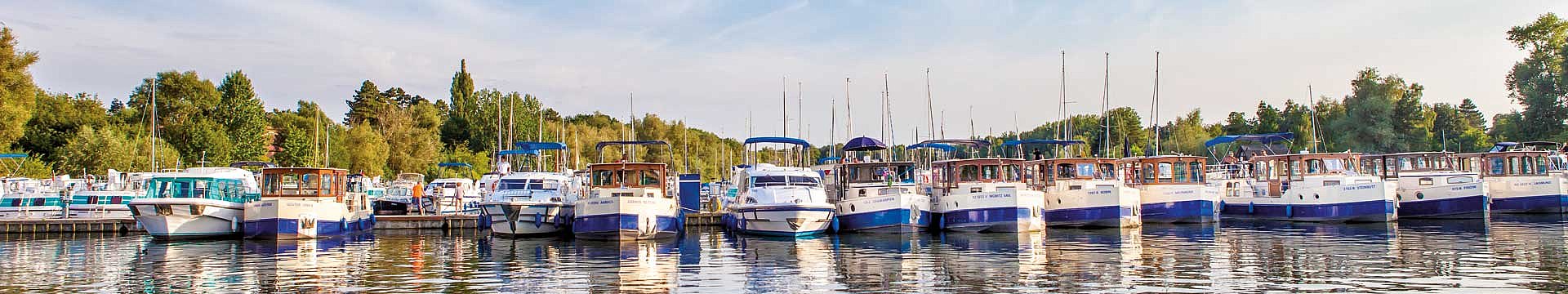 In einem Hafen stehen zahlreiche Hausboote nebeneinander. Es handelt sich umBoote der Marke Kormoran.