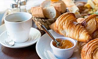 Ein Frühstück mit Kaffee, Croissant, Marmelade und weiteren leckeren Zutaten.
